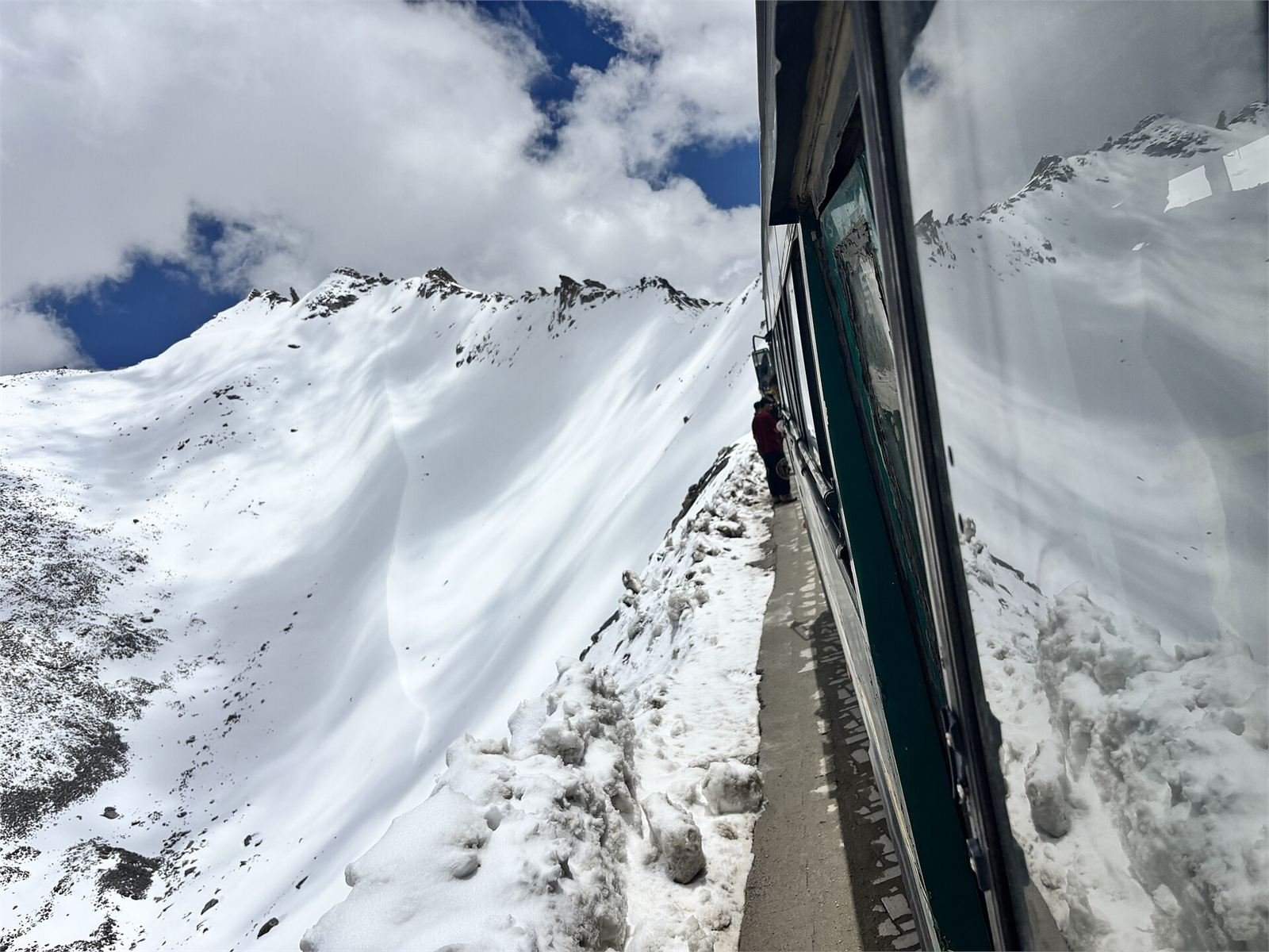 A vehicle edging along the snow-walled road at Khardung La under a blue sky