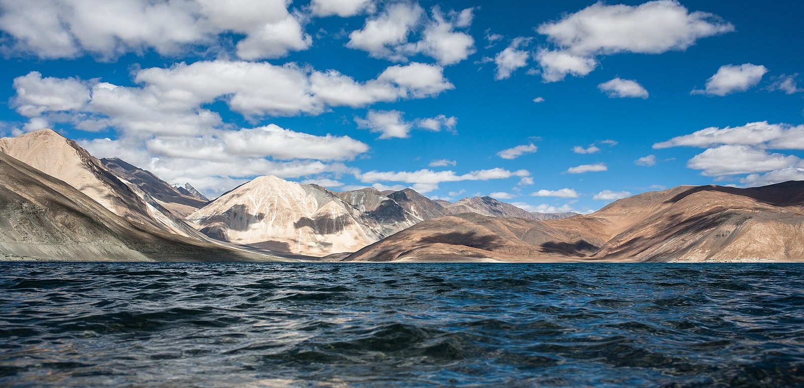 Pangong Tso's dark blue water below bare ochre mountains
