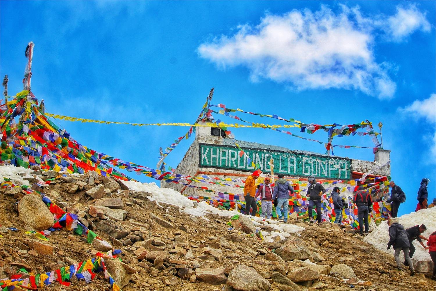 Prayer flags and the Khardung La Gonpa at the pass summit, snow and rock all around