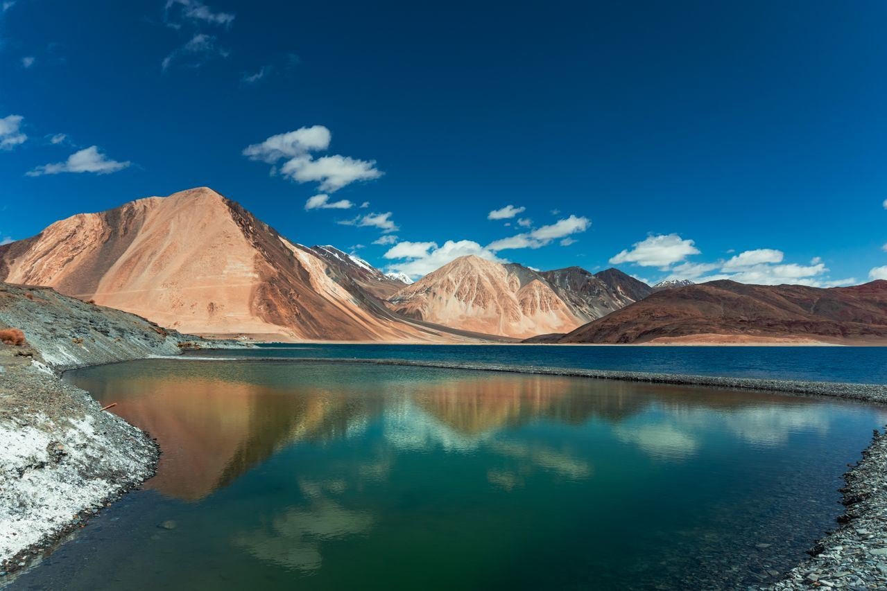 Pangong Lake's turquoise water mirroring bare ochre mountains under a deep blue sky